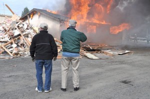 Oktoberfest board members John Gooley and Jerry Lauzon watch as the last vestiges of the original structures on the community building grounds go up in smoke