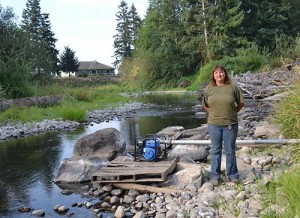 Melody Harpole standing on the bank of a very low Abiqua Creek. She normally irrigates her farm from the creek. This year’s drought will probably cause the loss of young fruit trees, she said. 